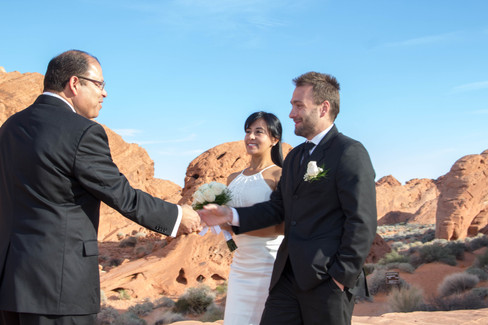 Oficiante de bodas dándole la mano al novio que llega con la novia mientras los recibe para celebrar su matrimonio en el desierto de nevada