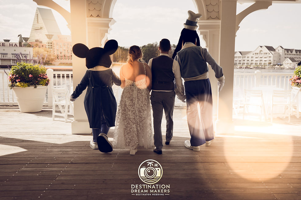A magical wedding moment as the bride and groom walk together with Mickey and Goofy overlooking a picturesque lakeside view.