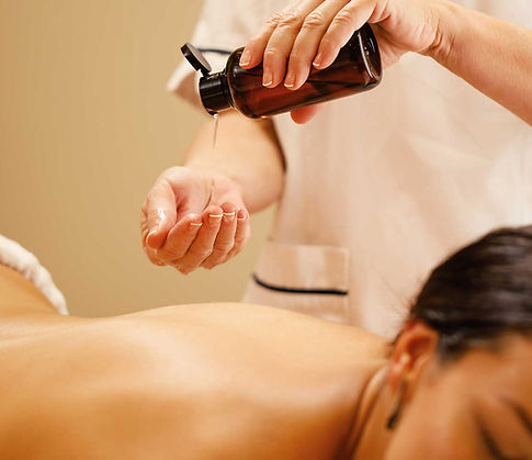 A professional masseuse at ZenVida spa pours warm essential oil from an amber bottle onto a client’s hands during a relaxing body massage session.