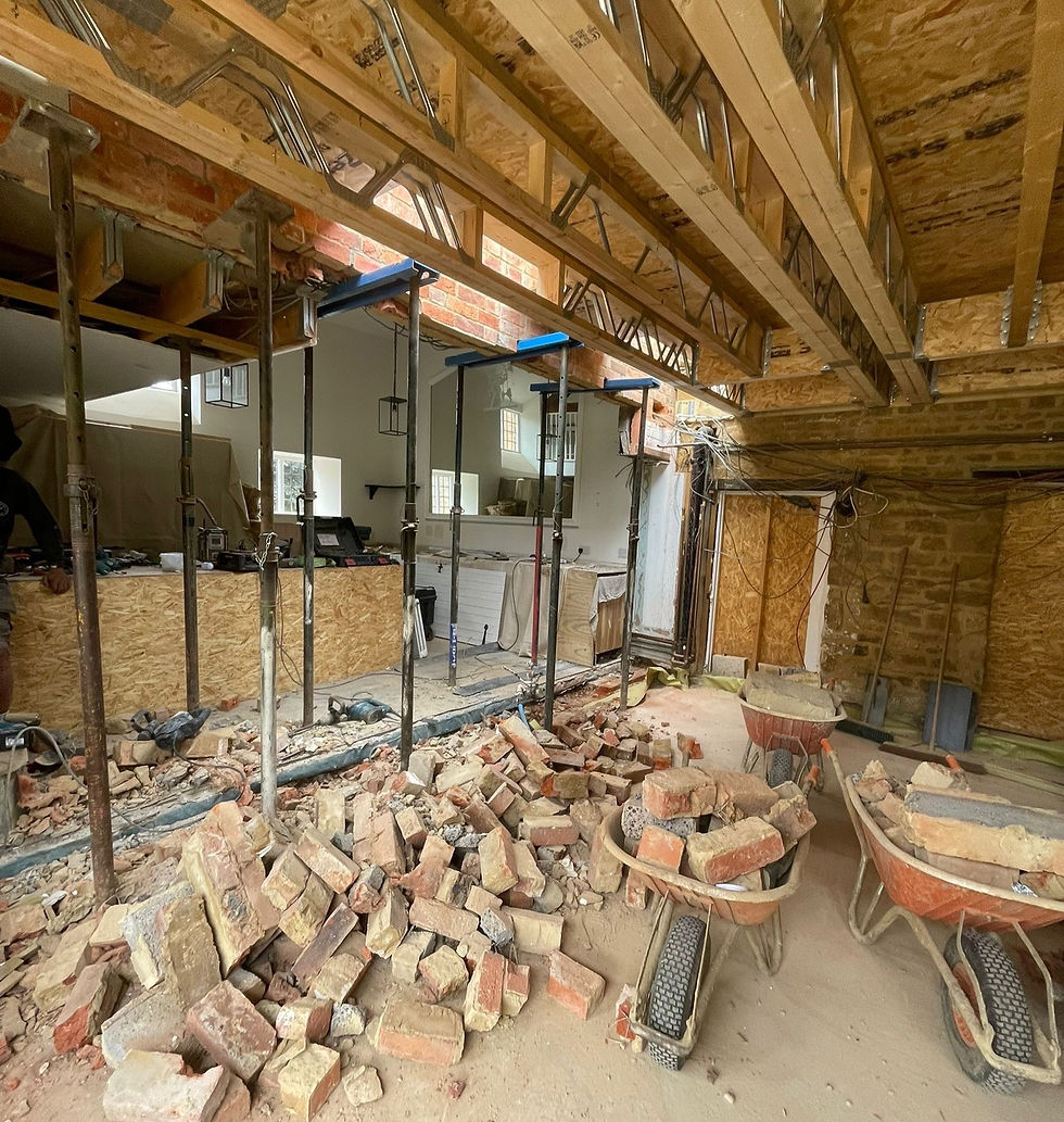 “Kitchen renovation in progress with exposed bricks, wheelbarrows, and boarding during wall removal”