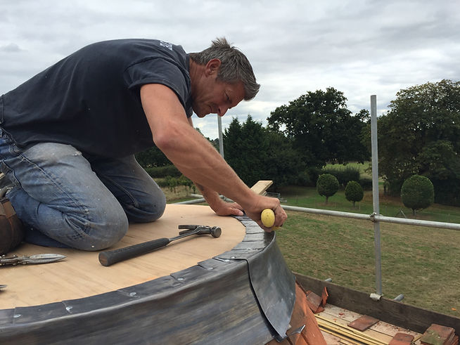 A skilled G&S craftsman performing expert oast cowl repair by carefully shaping lead flashing on a traditional Kent roundel roof.