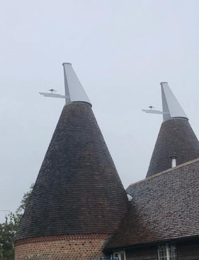Two pristine white oast cowls equipped with custom kangaroo finials, safely mounted on large traditional tiled roundel roofs.