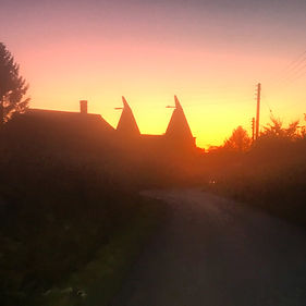 A striking sunset silhouette of a traditional heritage oast house with two wooden cowls in the countryside.