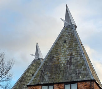 A traditional square kiln oast house featuring two white wooden cowls against a cloudy sky, highlighting listed building roof repairs in Battle.