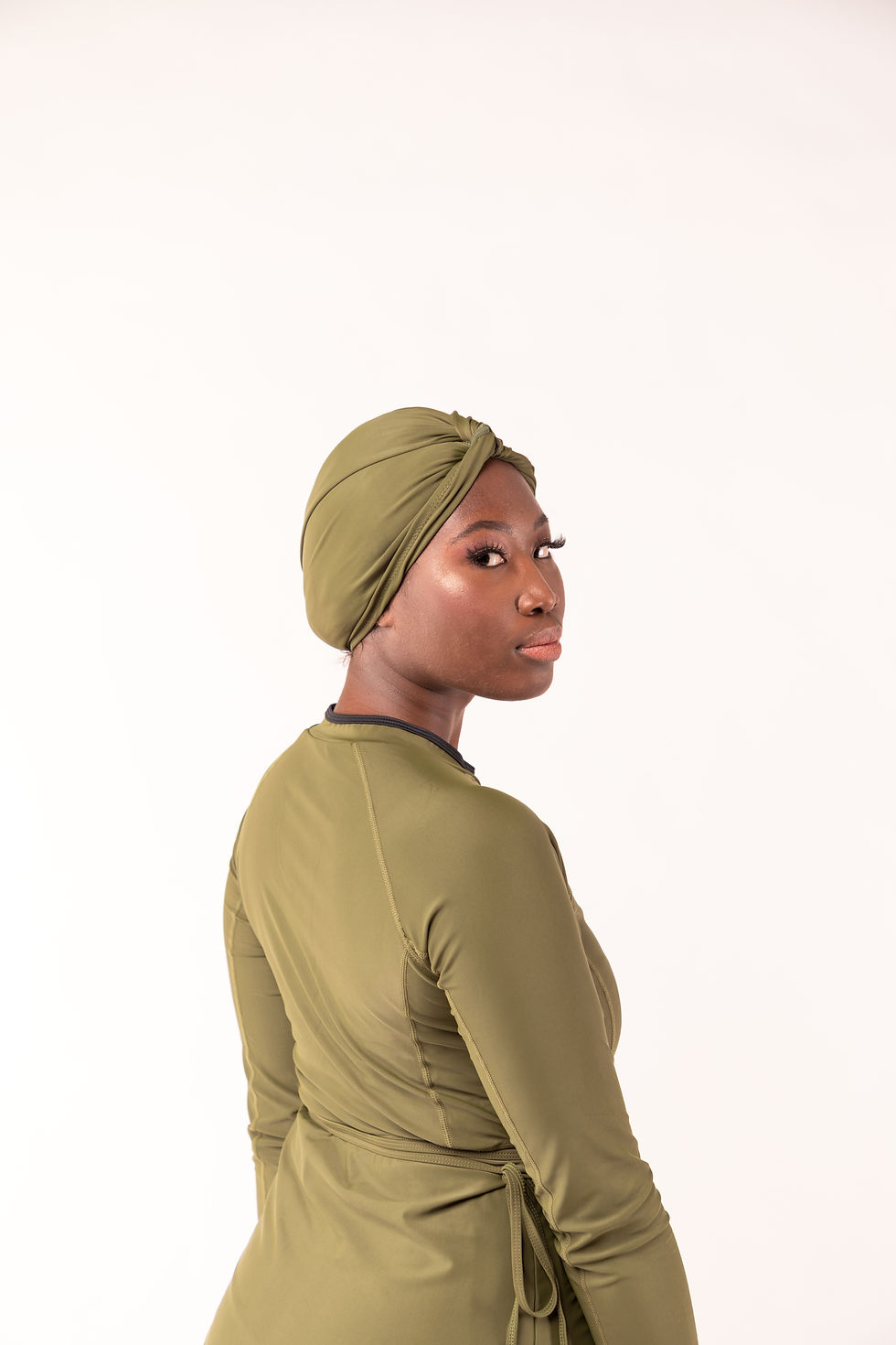 Thumbnail: femme de dos la tête tournée vers nous qui porte un turban de bain vert olive et un burkini assorti