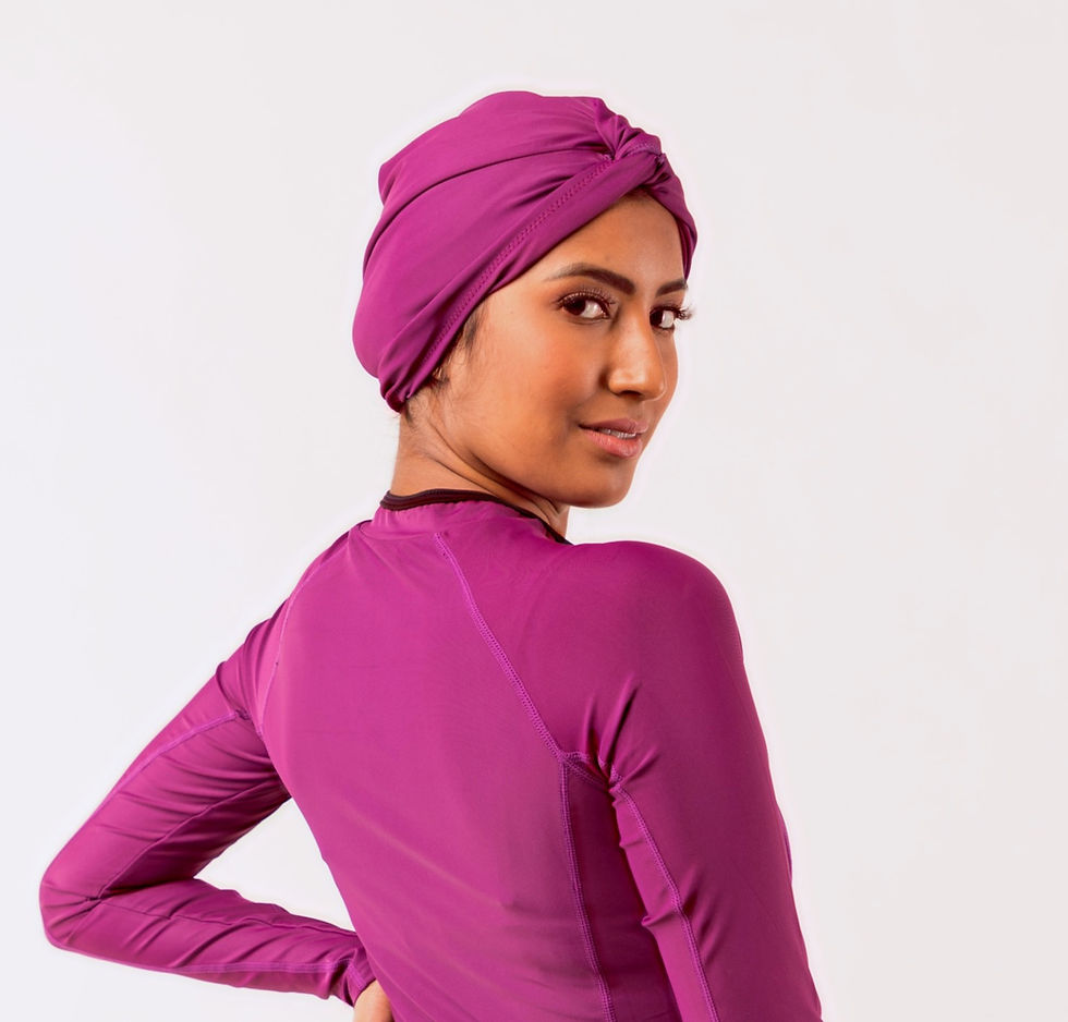 Thumbnail: femme de dos la tête tournée vers nous qui porte un turban de bain rose et un burkini assorti