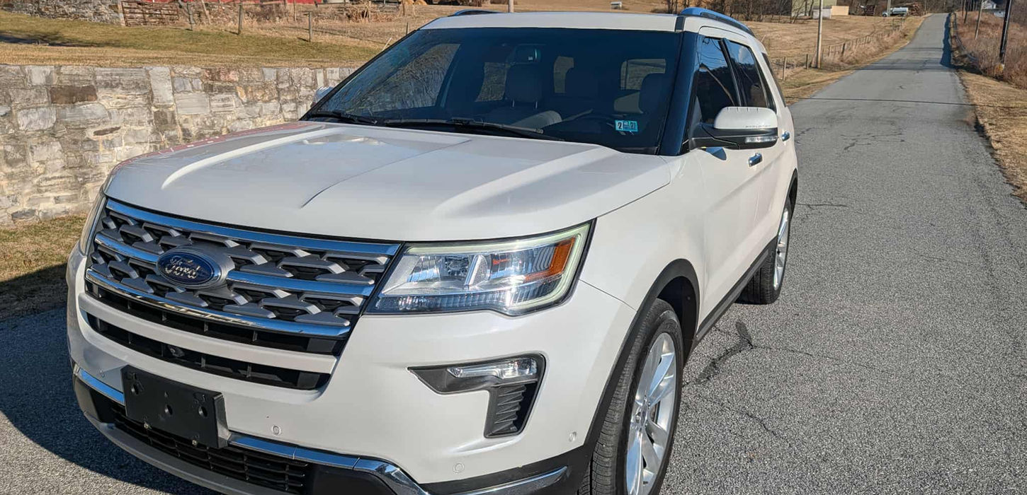 White SUV on a road with a red barn