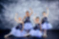 Four girls ages 5-11 striking a pose with one arm raised, wearing matching blue tutus with floral designs.