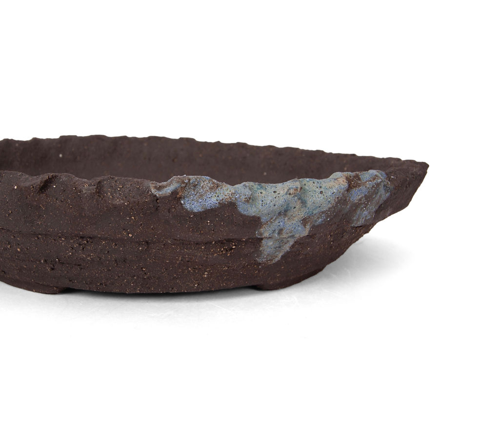 Ronde bonsai pot van grove zwarte klei met een lik donkergroene matte glazuur aan de rand, die ingeknepen is, detail