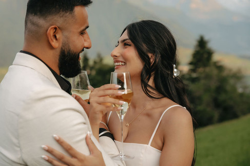 Couple smiling with champagne glasses in front of the hotel Villa Honegg on their marriage proposal photoshoot, in Switzerland