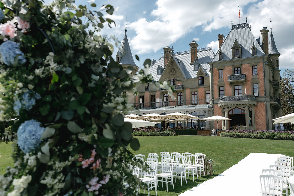 Elegant château garden setup : schloss schadau, with white chairs and umbrellas, floral arch in foreground, under a bright blue sky with clouds. Schloss Schadau wedding photographer Lake Thun Bernese Oberland, Switzerland.