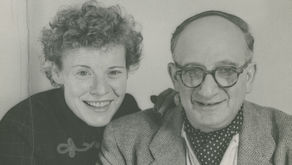Black and white photograph of Margret and H.A. Rey sitting side by side, smiling. 
