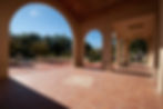Outdoor area oustide of library with tiled floor and open area with covering. Around the covered area are trees and other buildings.