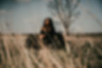 The creator of Lady Earth Design and Birth, sitting in a grass field wearing a black dress with a tree in the background.