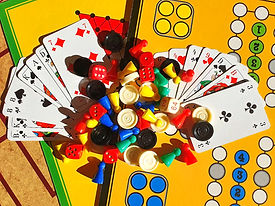 Bunte Spielsteine, Würfel und Karten auf gelbem Brettspielhintergrund.