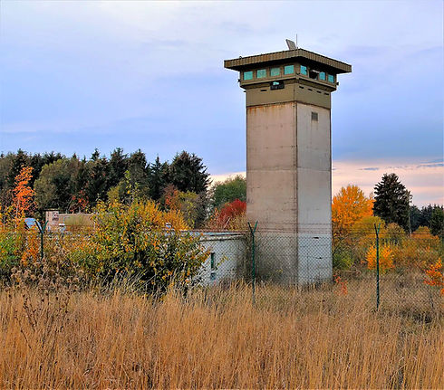 Konkreter Wachturm in herbstlicher Landschaft mit trockener Wiese unter bewölktem Himmel.