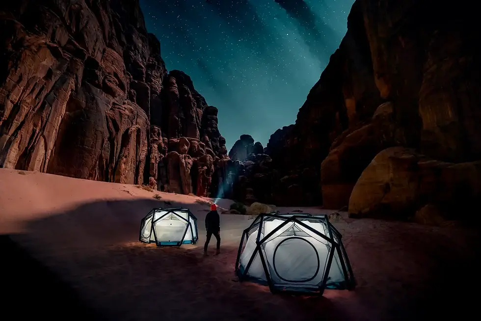 Person mit Taschenlampe zwischen zwei Zelten in dunklem Wüstencanyon.