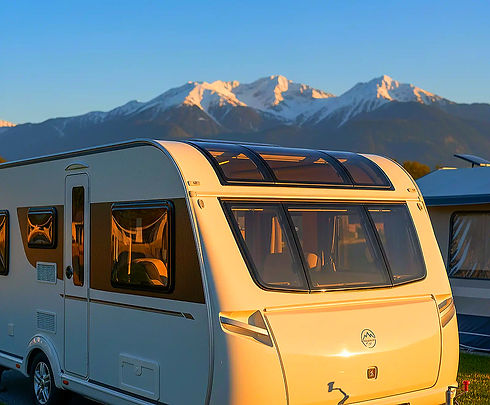 Weißer Wohnwagen - Camping vor schneebedeckten Bergen im goldenen Sonnenlicht.