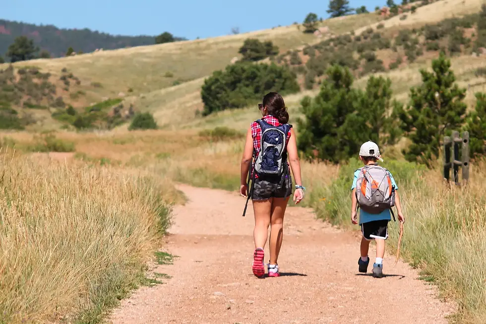Frau und Kind wandern mit Rucksäcken auf einem sonnigen Feldweg.