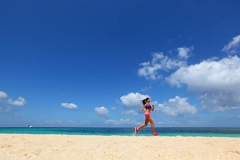 Junge Frau joggt am tropischen Strand unter blauem Himmel, Ausdauertraining.