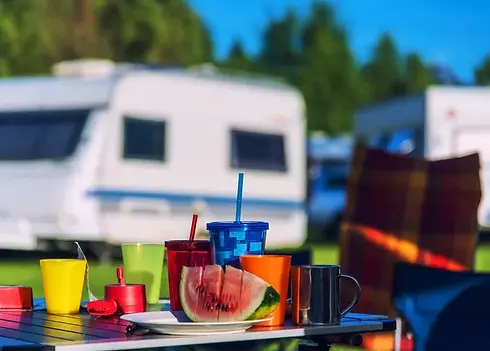 Camping scene with cups, watermelon, and caravan in the background. Vagabundo