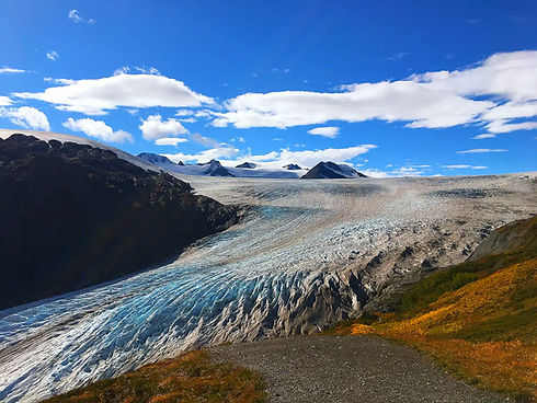 Mächtiger Gletscher schlängelt sich durch alpine Landschaft unter blauem Himmel.