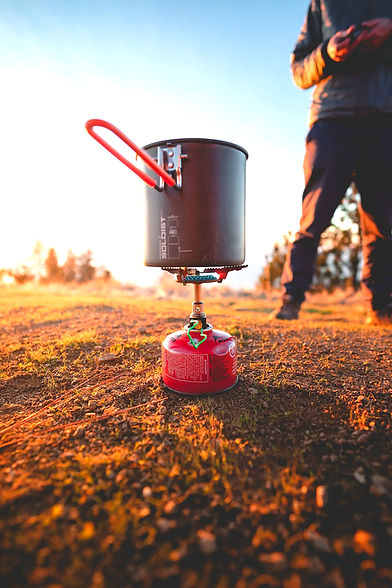 Kochtopf auf Gaskocher draußen bei Sonnenuntergang, essentielle Camping Ausrüstung.