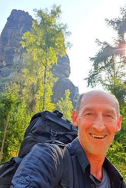Mann lächelt mit Rucksack vor Baum, Berg, sonniges Licht, Mike Gnuechtel Gründer Vagabundo