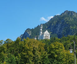 Schloss Neuschwanstein, ein Schloss auf einem Hügel, umgeben von Bäumen und blauem Himmel.