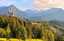 Skisprungschanze in grüner Gebirgslandschaft unter blauem Himmel; Outdoor-Abenteuer.