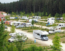 Campingplatz mit vielen Wohnwagen und Wald im Hintergrund. Vagabundo Ihr Outdoor Experte