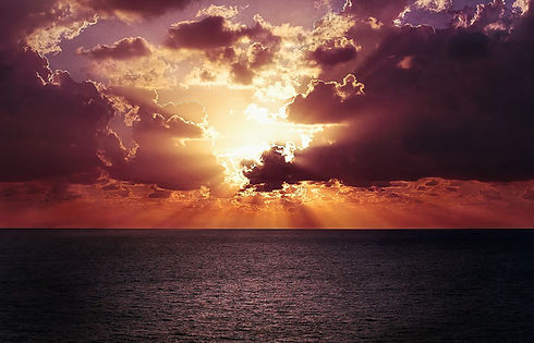 Dramatischer Sonnenuntergang über dem Meer, Sonnenstrahlen durchbrechen dunkle Wolkenformationen.