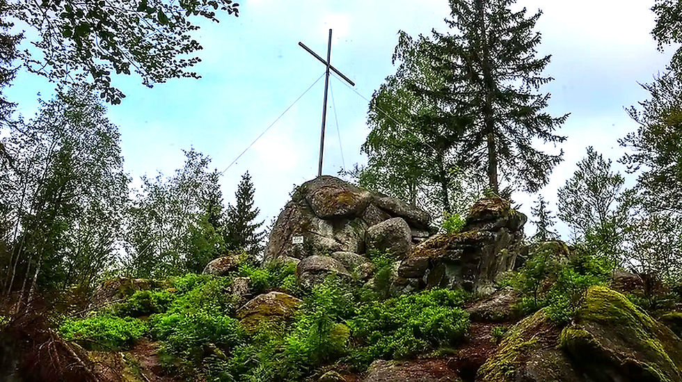Ein Kreuz steht auf einem Felsen, Naturpark Fichtelgebirge, umgeben von Bäumen.
