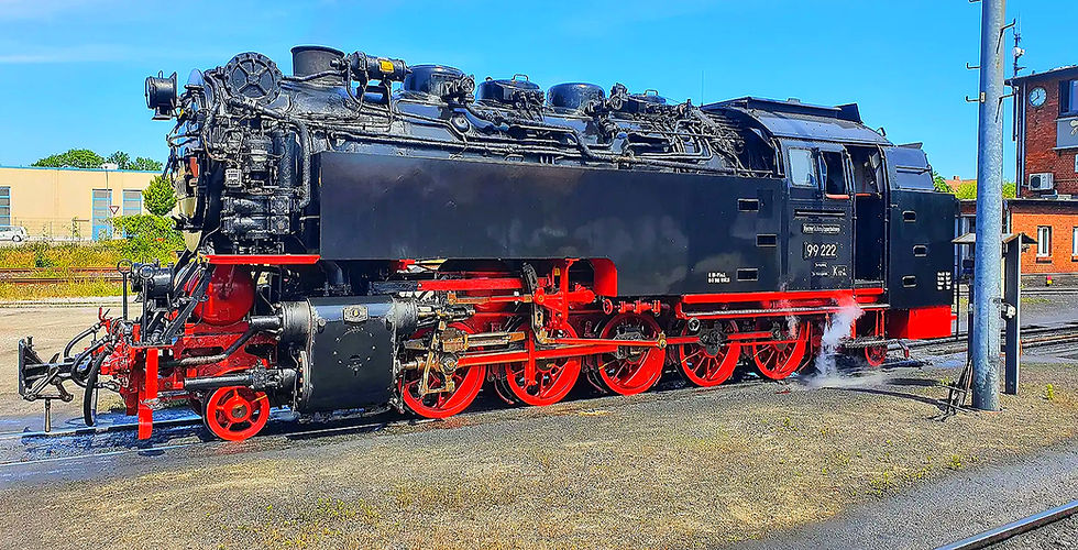 Schwarze Dampflokomotive mit roten Rädern parkt auf einem Gleis im Freien.