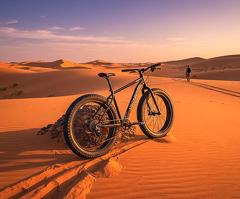 Fahrrad im Sand der Wüste, eine Person im Hintergrund, warme Farben.