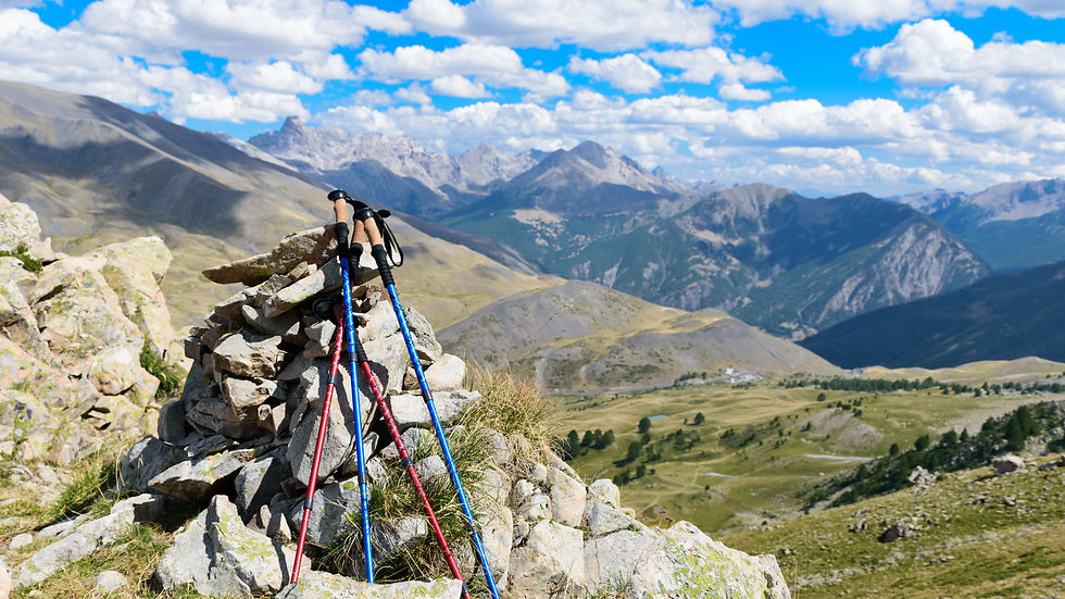 Wanderstöcke auf einem Steinhaufen vor einer Berglandschaft mit blauem Himmel.