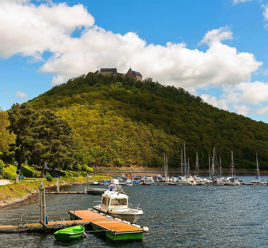 Boote im Edersee mit Schloss Waldeck auf grünem Hügel unter blauem Himmel.