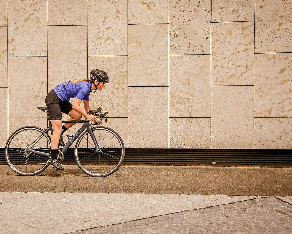 Radfahrerin in Fahrradbekleidung mit Helm fährt Rennrad vor heller Wand.