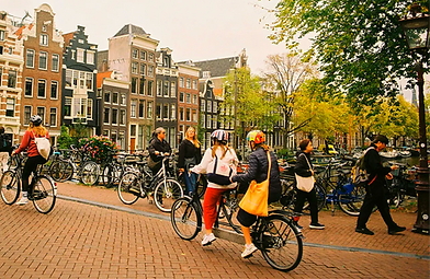 Menschen fahren Fahrrad über eine Amsterdamer Brücke vor Grachtenhäusern.