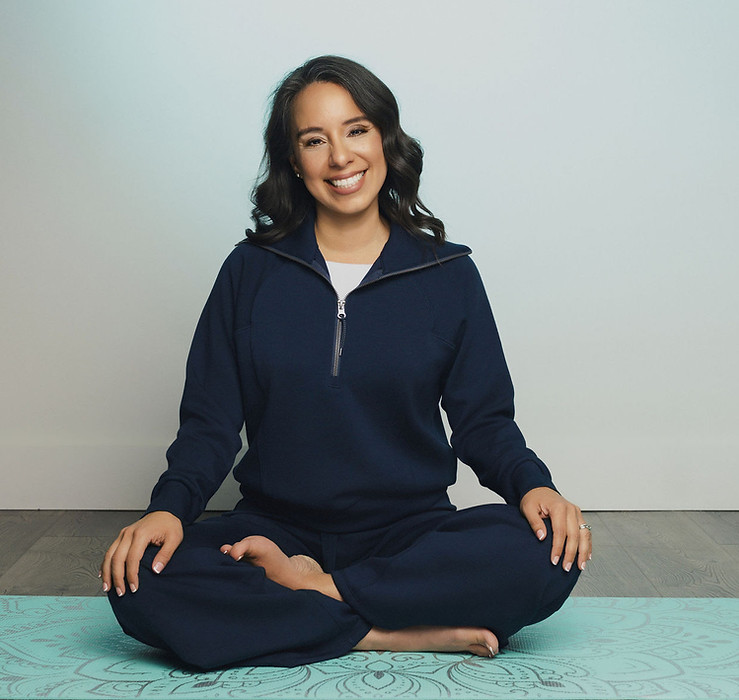 Instructor Sonia sitting down on a yoga mat smiling