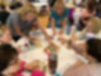 People stand around a circular table, building with craft materials.