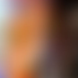 Two women smiling in front of a colorful floral mural with red, blue, and yellow flowers. One wears a paint-splattered jumpsuit. Urban setting.