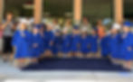 A row of preschoolers in graduation caps and gowns stand, holding their hands over their hearts.