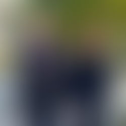 Two people in suits smiling outside, standing by a white fence and green bushes. Background shows a house with blue shutters.