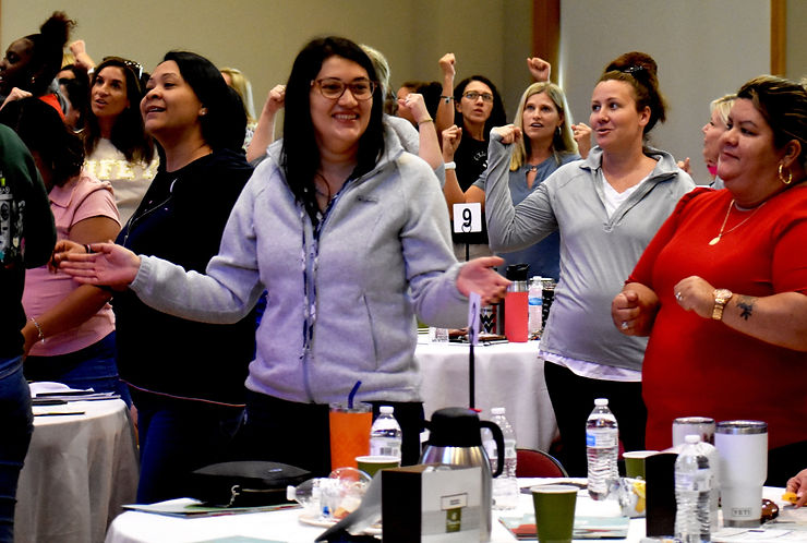 An audience of women stand, clapping their hands.
