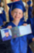 A preschooler, dressed in graduation cap and gown, holds up a certificate