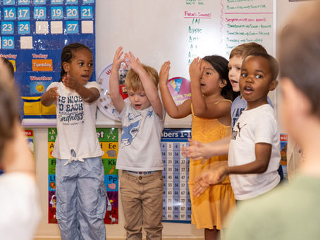 Children joyfully clap in a classroom, surrounded by colorful educational posters and charts. Emphasis on teamwork and happiness.