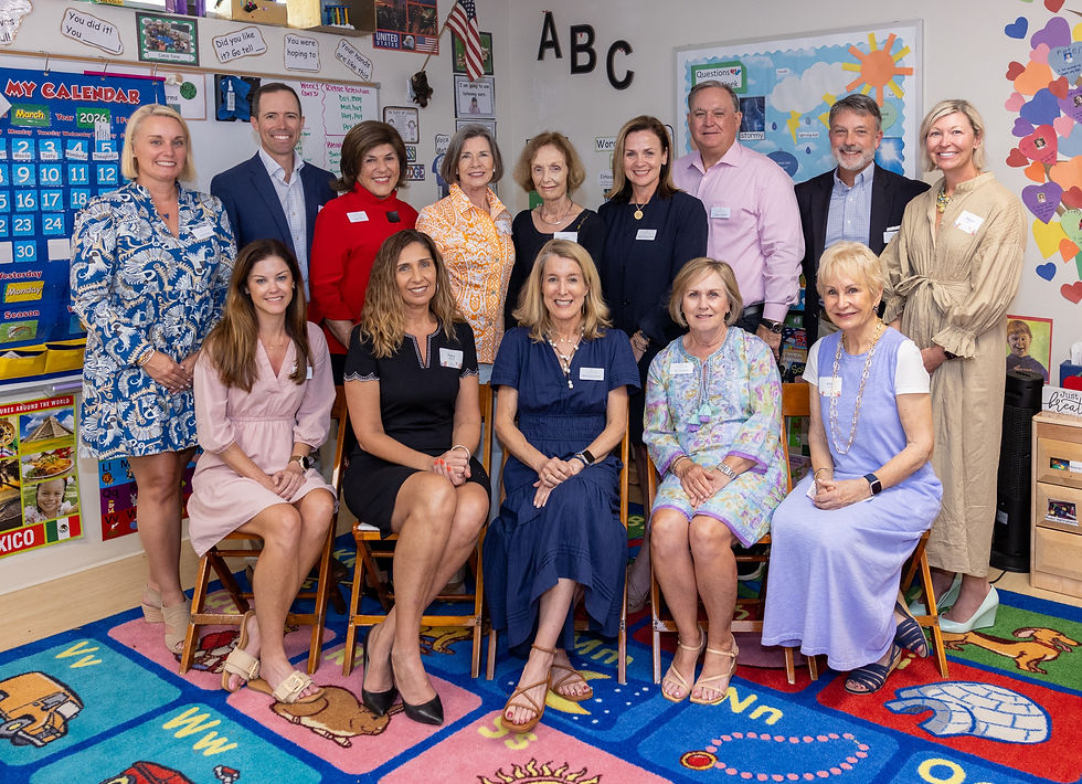 A group of adults poses in a colorful classroom with educational posters and ABC letters. They are smiling and dressed in various outfits.