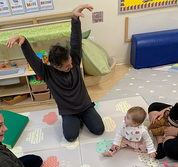 Man playfully gestures at a baby on a patterned mat in a cozy playroom.