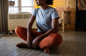 A woman sits on the floor while smiling and meditating. This could represent a coping skill learned by working with a trauma therapist in Baltimore, MD. Search for "healing from trauma in Baltimore, MD" to learn more about trauma therapy in Pikesville, MD today.